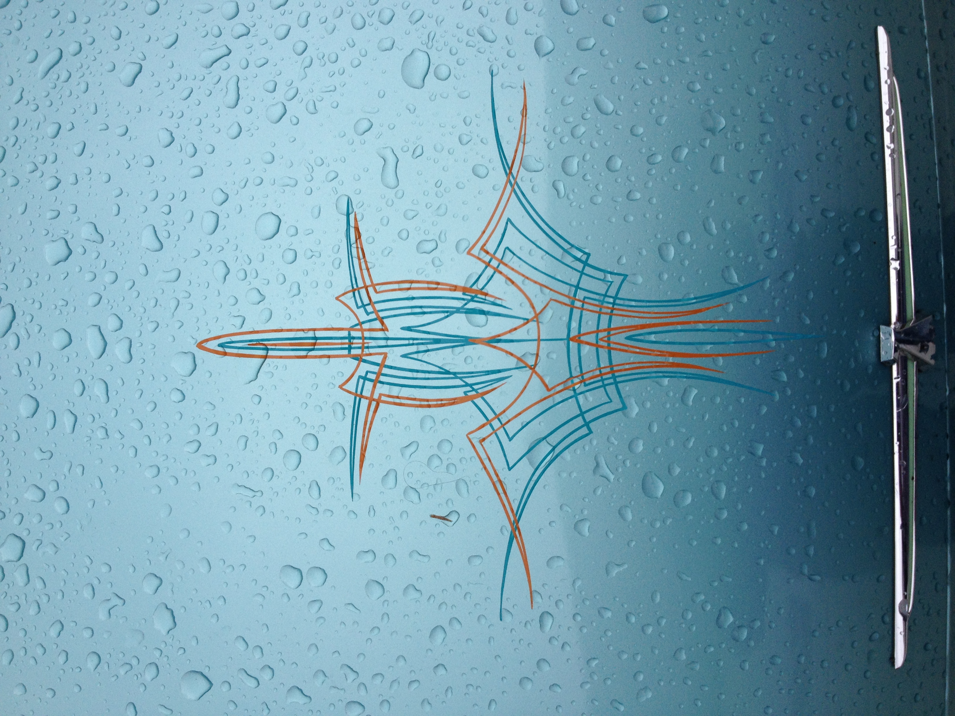 Teal and orange pinstripe star design on a rain-speckled car panel